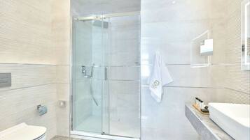 A modern bathroom with a glass-enclosed shower, a toilet, and a vanity with a bathtub.