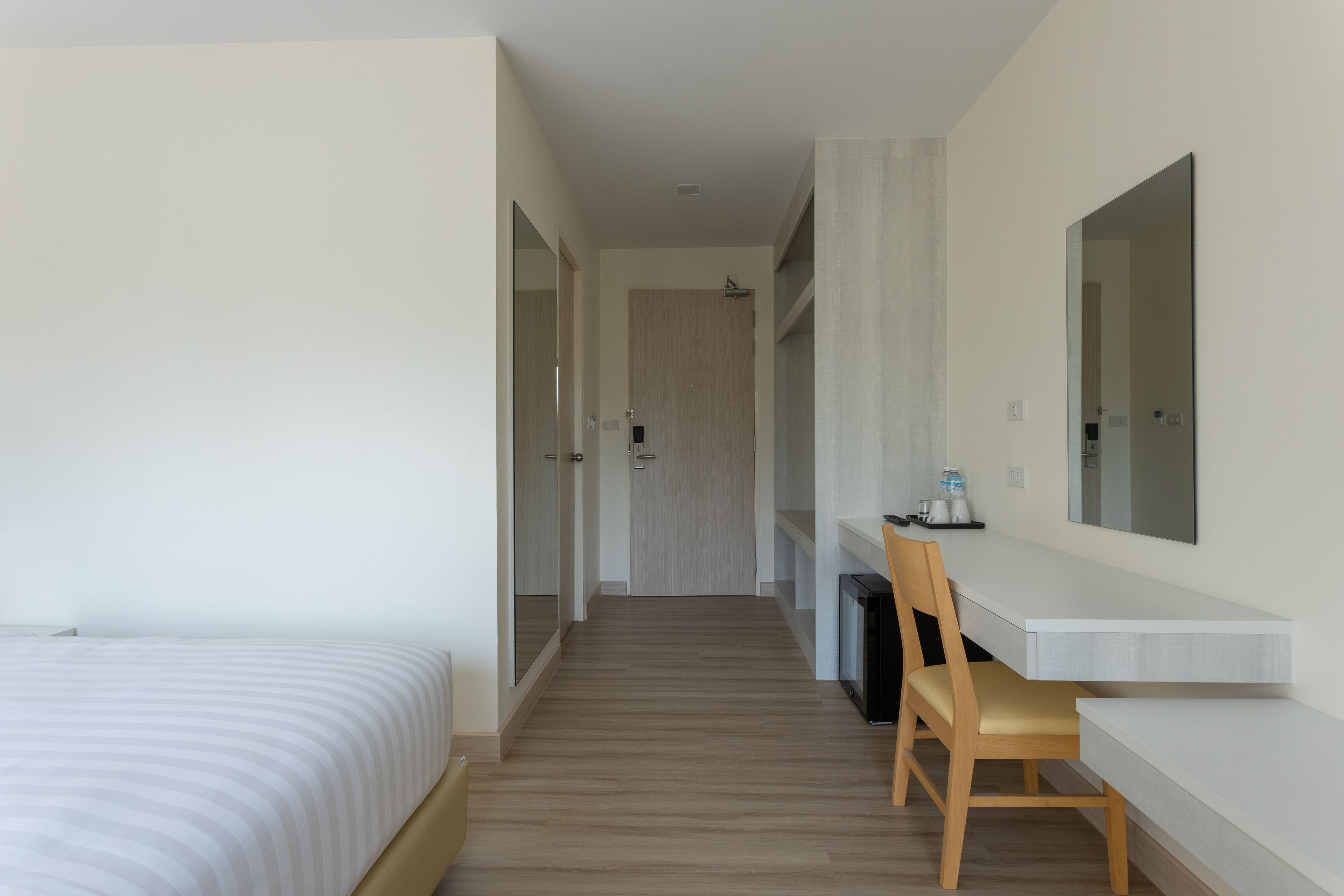 Una habitación de hotel con cama, escritorio y silla, espejo y puerta que da a otra habitación.