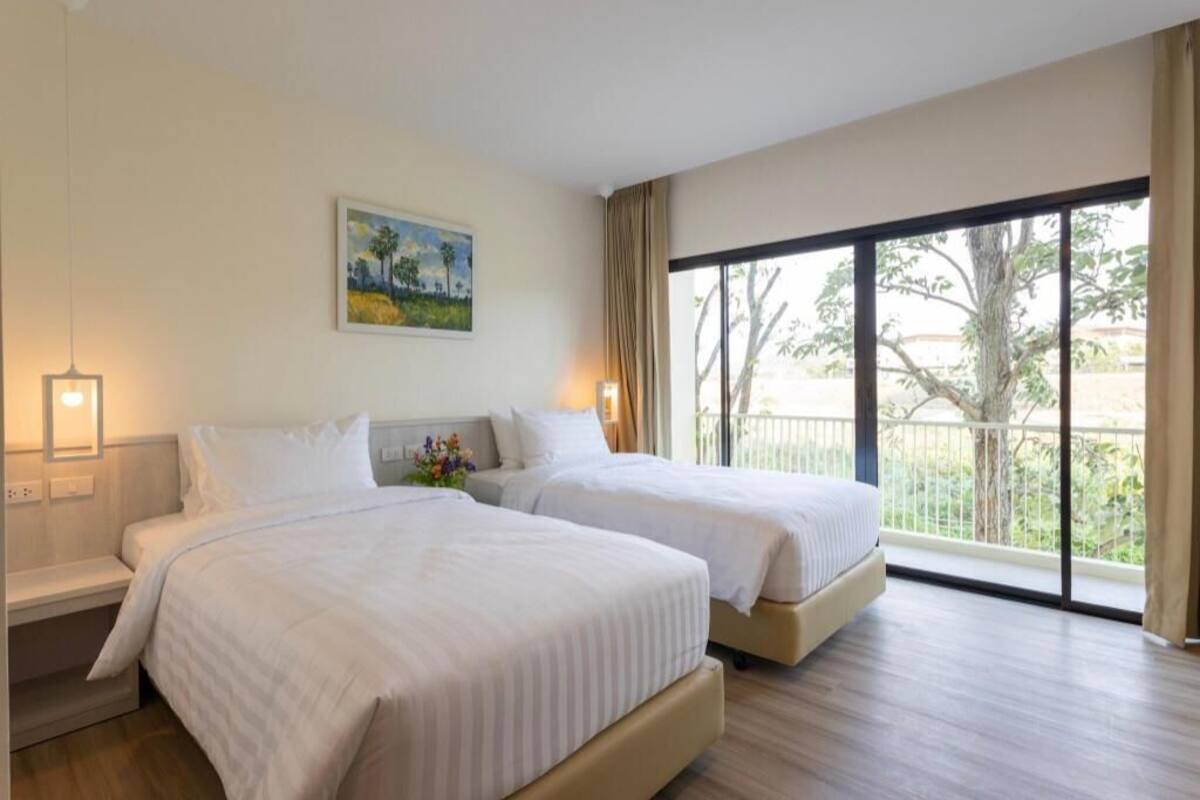A hotel room with two beds, a painting on the wall, a nightstand, and a large window with a view.
