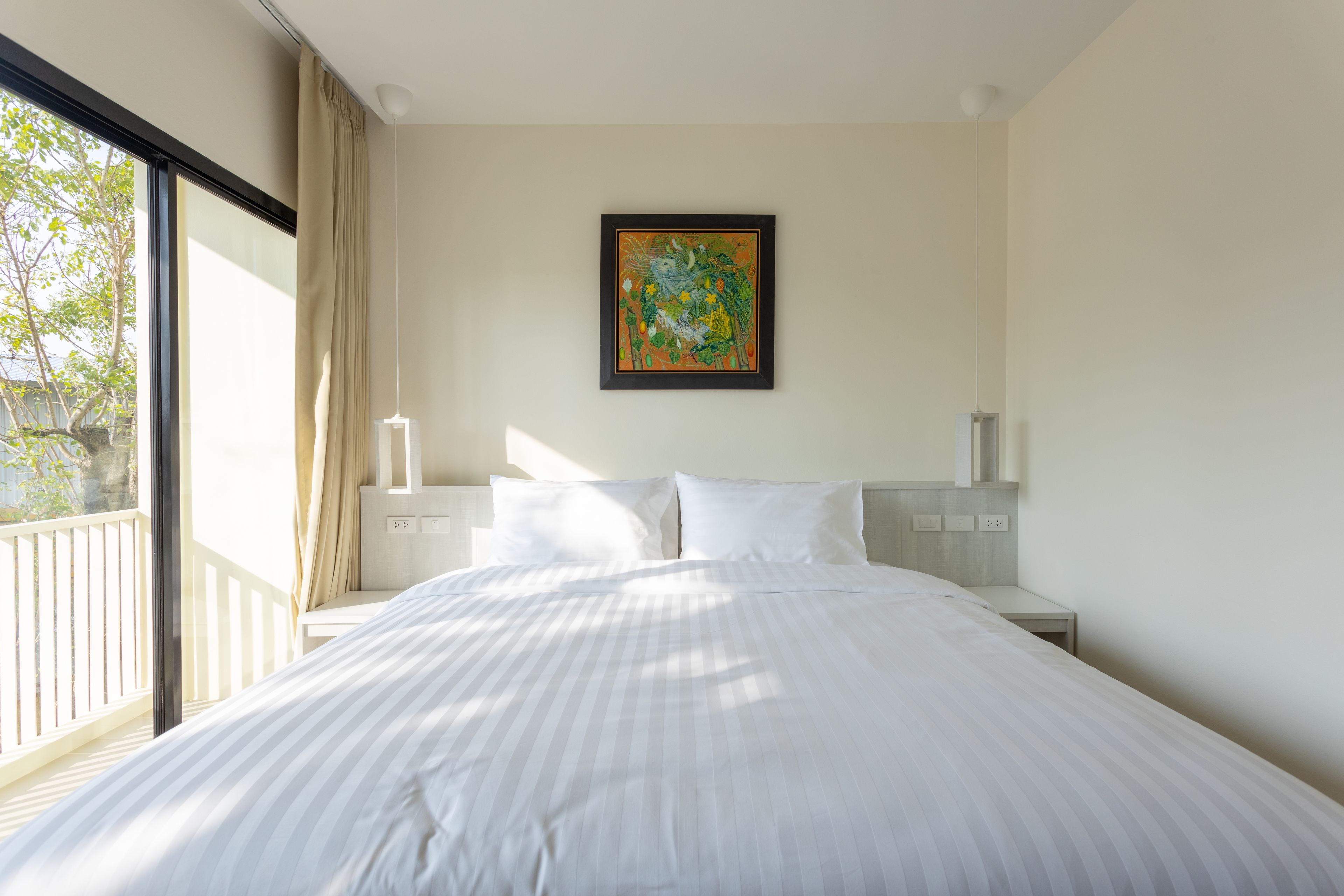 Habitación de hotel con una cama grande, una mesita de noche, una obra de arte enmarcada en la pared y vistas al exterior a través de una ventana.