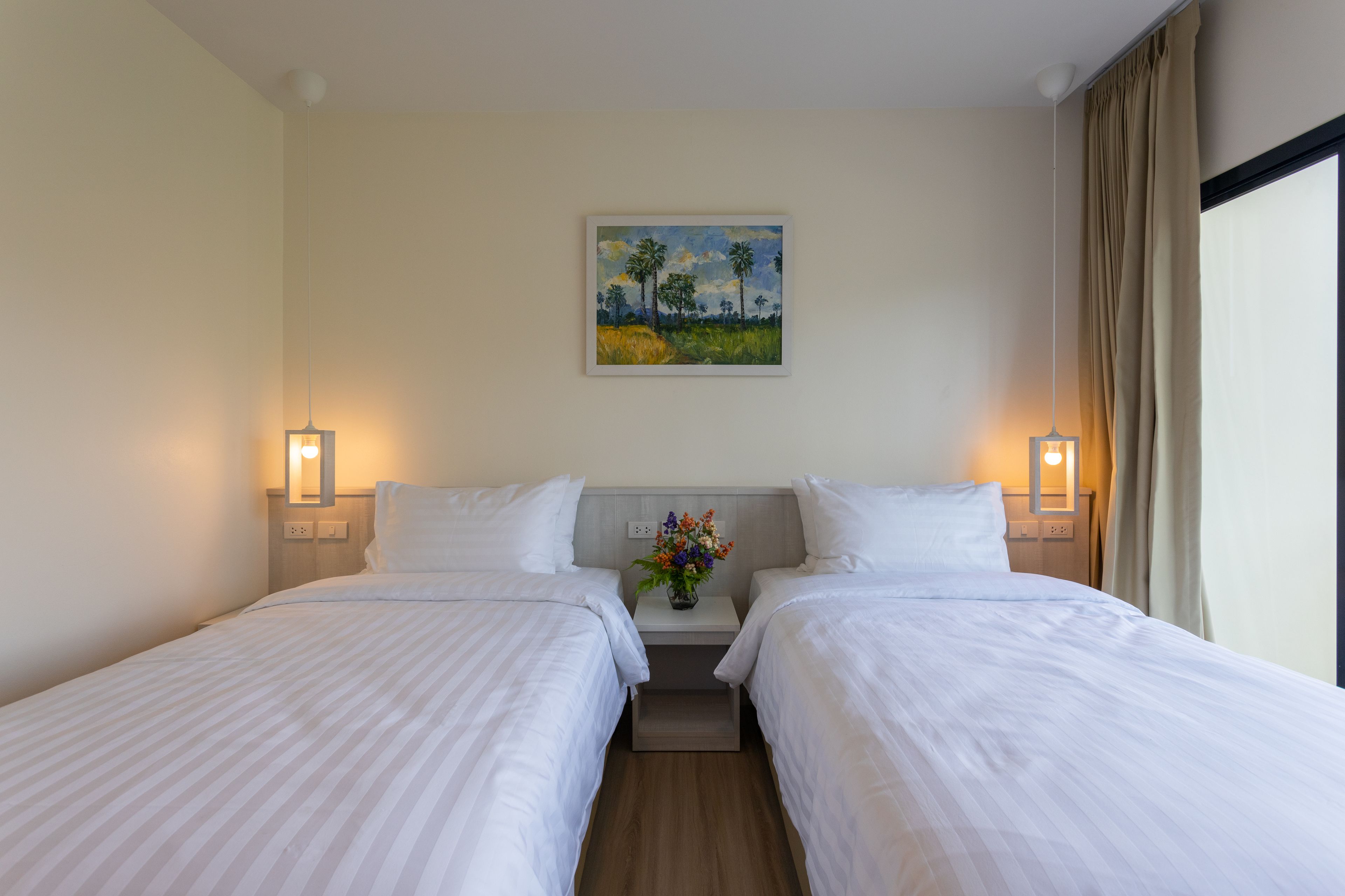 Una habitación de hotel con dos camas individuales, una mesita de noche con un jarrón de flores y un cuadro en la pared.