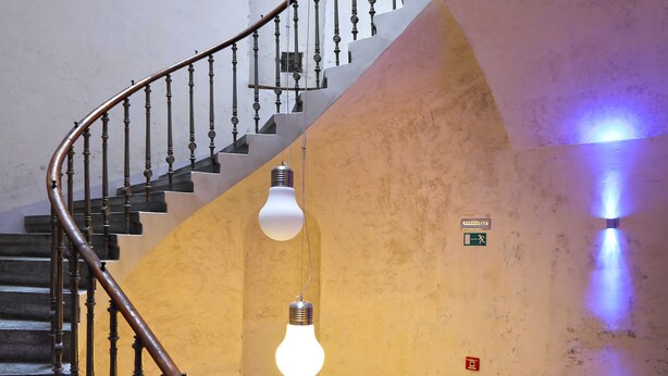 A spiral staircase with wooden railings and a handrail, leading to a landing with a light fixture and a sign. - Apartments At The Blue Duckling (Prague)