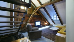 A loft-style room with exposed wooden beams, a television, a sofa, and a small table. - Apartments At The Blue Duckling (Prague)