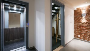 An elevator with a modern design, a hallway with a brick accent wall, and a staircase with wooden railings. - Apartments At The Blue Duckling (Prague)