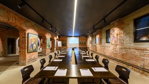 Un salón de conferencias con largas mesas y sillas, paredes de ladrillo y obras de arte en las paredes.