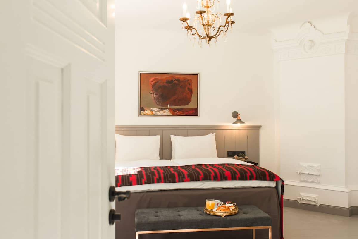 Una habitación de hotel con una cama, una mesita de noche, una bandeja con productos de desayuno y un cuadro en la pared.