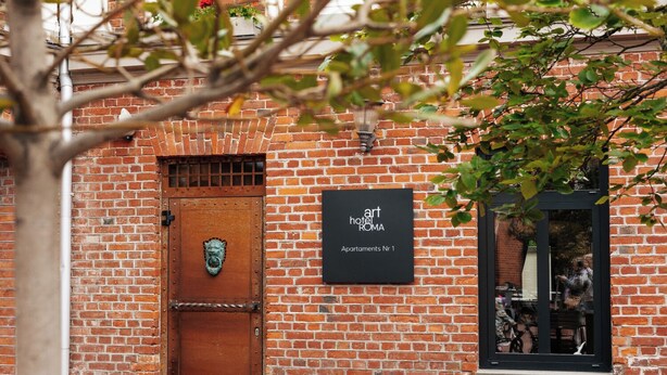 Un edificio de ladrillo con un letrero que dice 'art hotel ROMA' y una puerta marrón con un tirador con forma de cabeza de león.