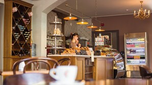 Interior de una cafetería con un barista preparando bebidas, una estantería de vinos y un dispensador de líquidos.