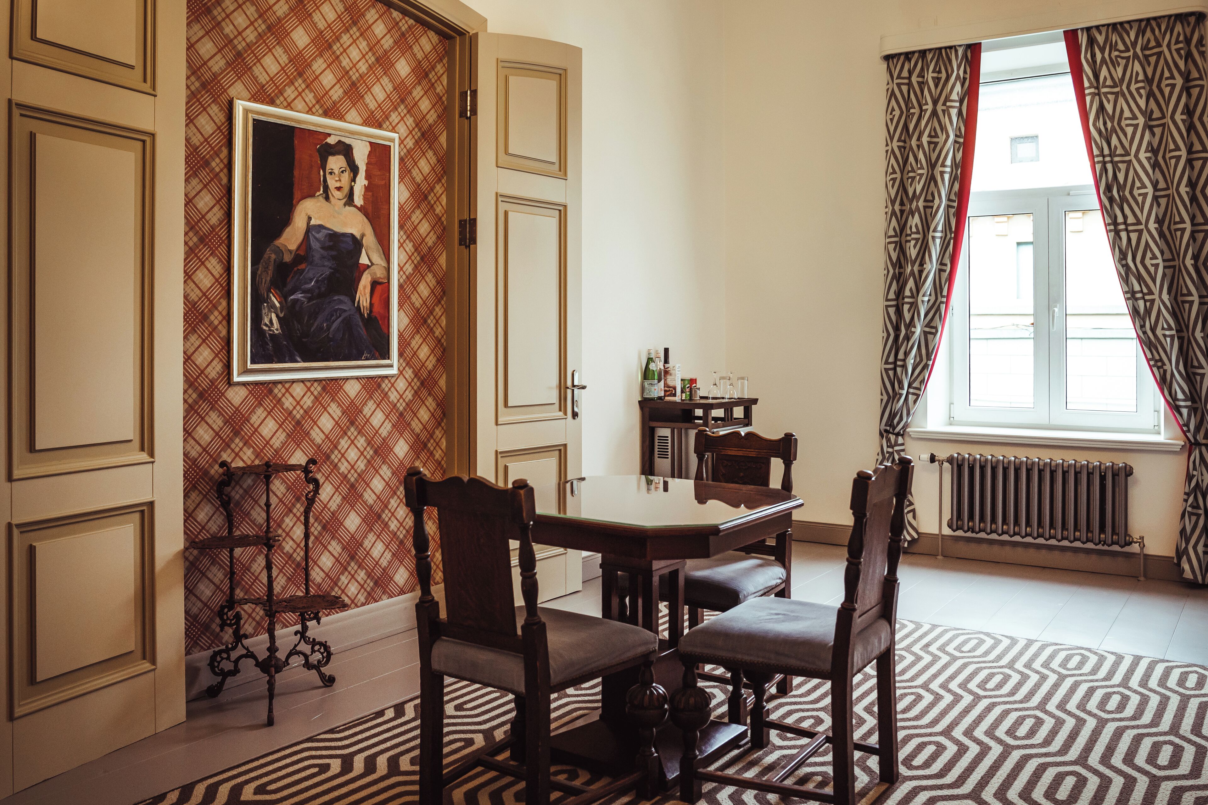 A dining area with a table and chairs, a painting on the wall, and patterned curtains.