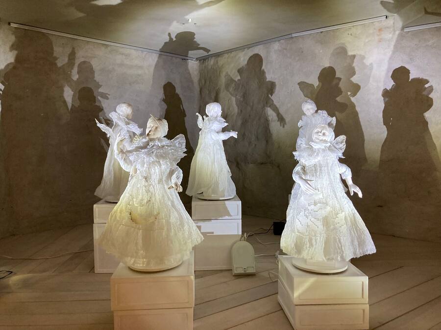 Una habitación con tres esculturas blancas sobre pedestales, una lámpara y una pared en sombra.
