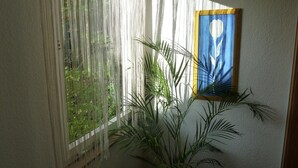 A room with a large window covered by sheer curtains, a framed artwork on the wall, and a potted plant. - Edelstein-Hotel (Idar-Oberstein)