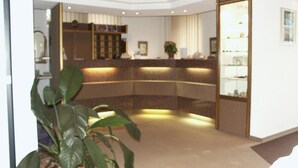 A reception area with a curved counter, a potted plant, and a bookshelf. - Edelstein-Hotel (Idar-Oberstein)