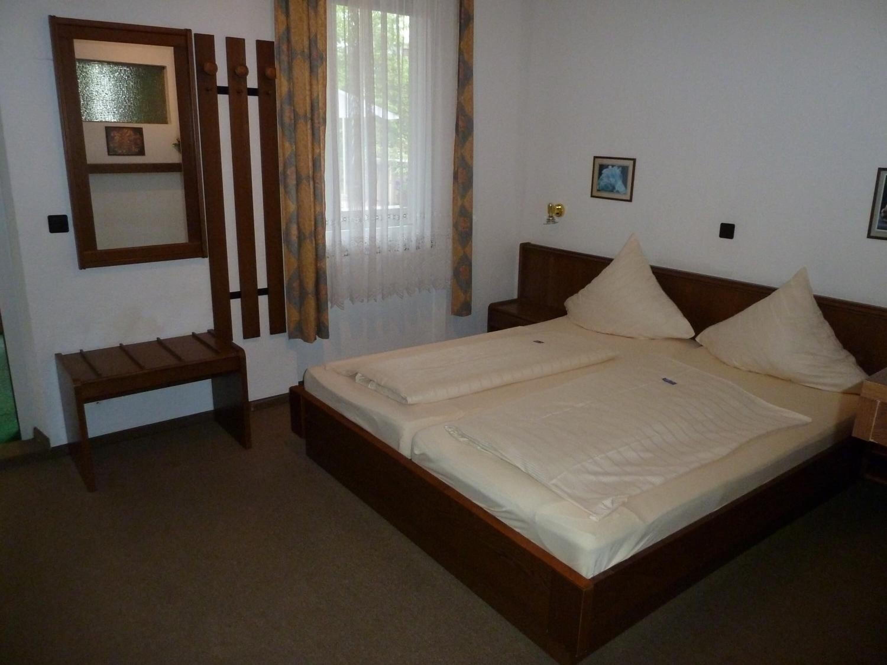 A bedroom with a double bed, a bedside table, a mirror, and a window with curtains.