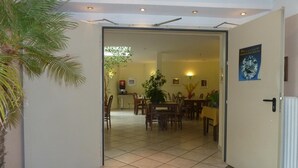 A hotel room with a tiled floor, a dining area with chairs and a table, and a large potted plant. - Edelstein-Hotel (Idar-Oberstein)