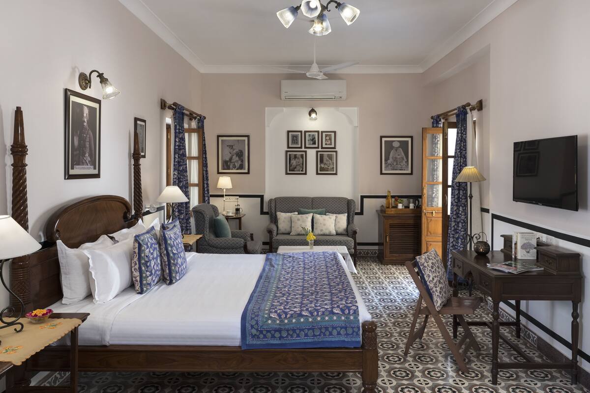 A hotel room with a large bed, a sofa, a desk, a television, and a ceiling fan.