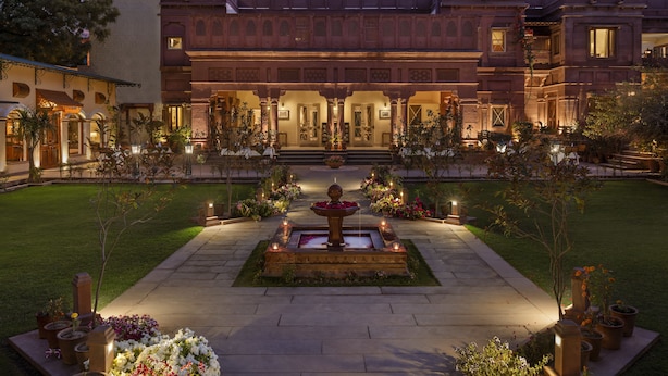 A large, ornate building with a central courtyard, featuring a fountain, potted plants, and a well-maintained lawn.