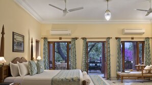 A spacious bedroom with a large bed, a wooden nightstand, a reading chair, and a view of the outdoors through a glass door.