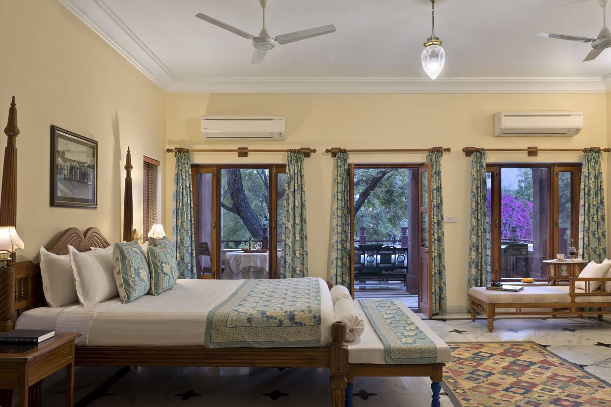 A spacious bedroom with a large bed, a wooden nightstand, a reading chair, and a view of the outdoors through a glass door.