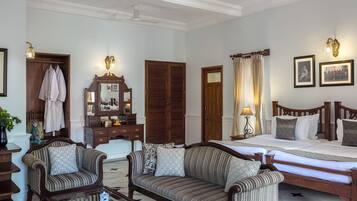 Une chambre d’hôtel bien aménagée, dotée d’un grand lit, de deux canapés, d’une commode en bois, d’un miroir et d’un ventilateur de plafond.