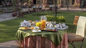 An outdoor dining table set with breakfast items, a pitcher of orange juice, and a view of a traditional building with a garden in the background.