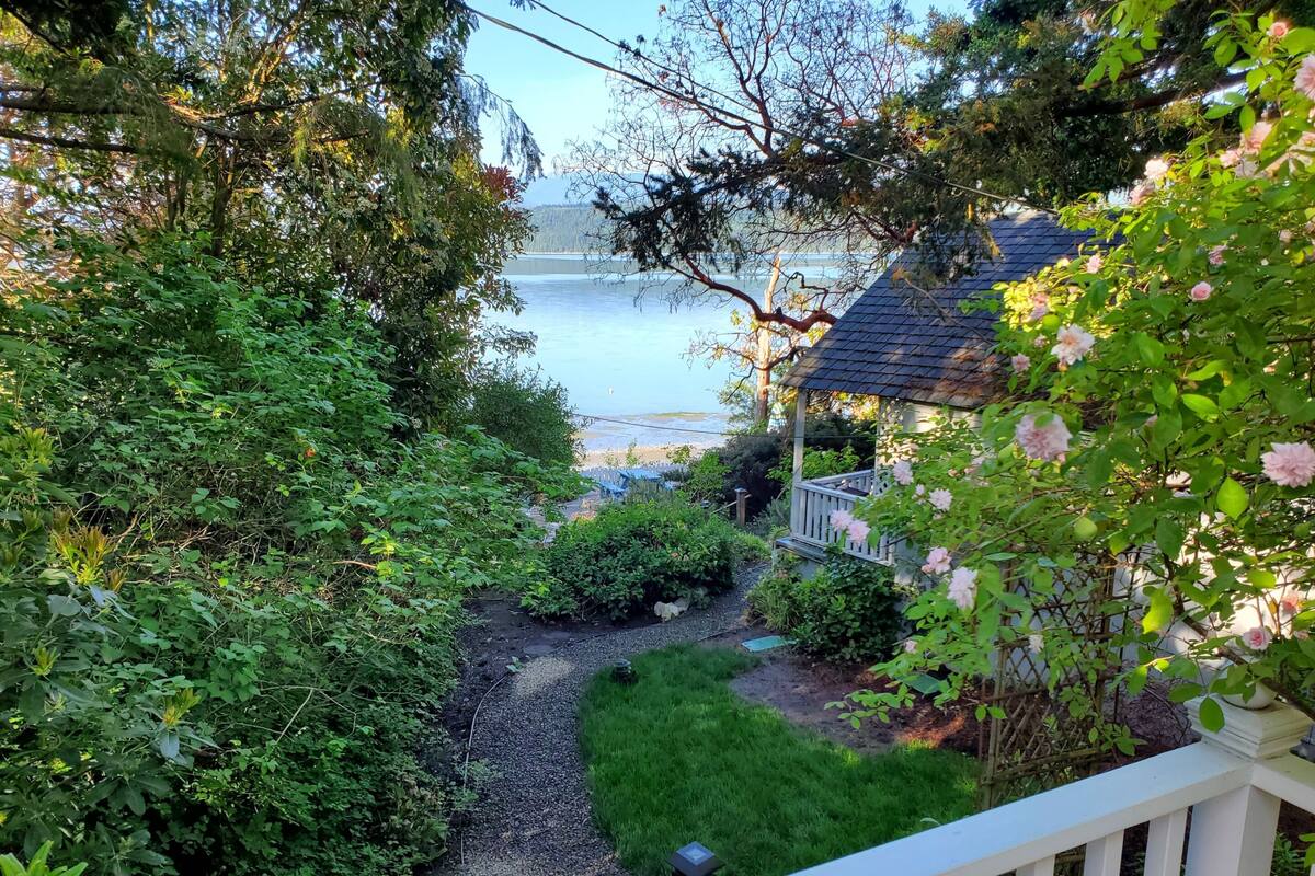 A garden pathway leading to a house with a view of a lake.