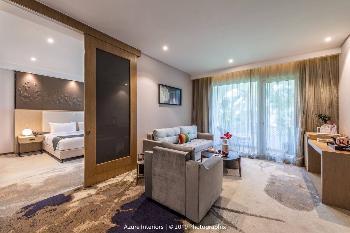 Una habitación de hotel moderna con cama, sofá, escritorio y un gran ventanal con cortinas.