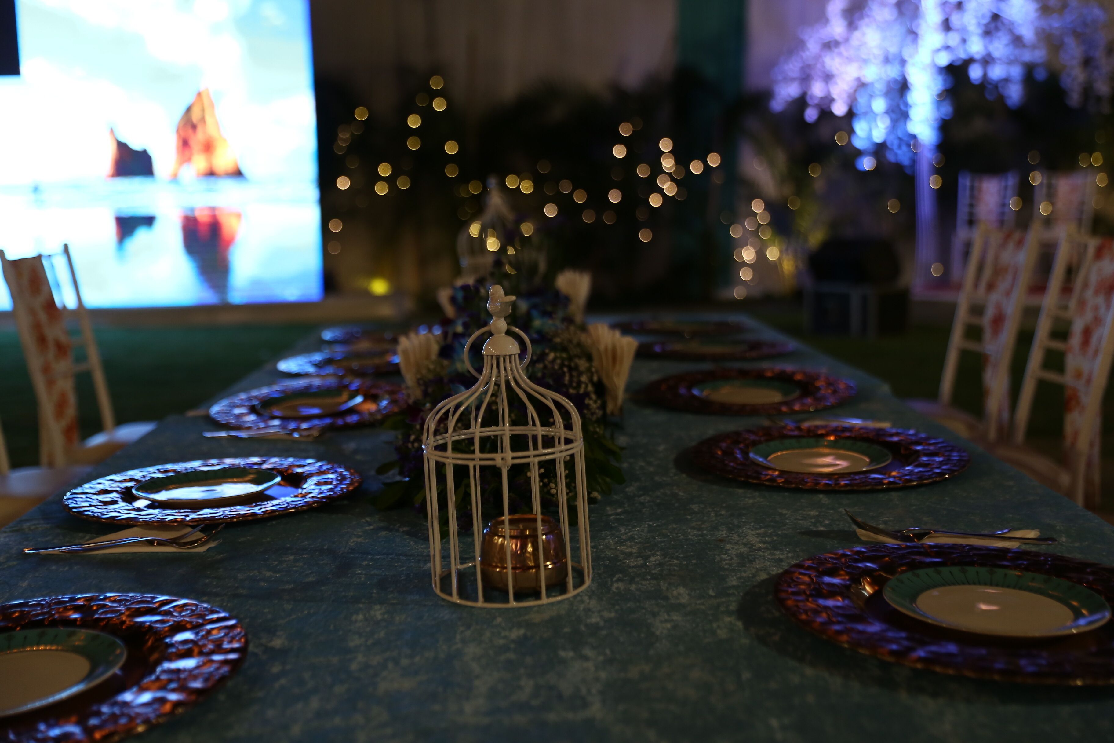Une table dressée avec des assiettes, des couverts et une bougie, dans une pièce faiblement éclairée et décorée de guirlandes lumineuses.