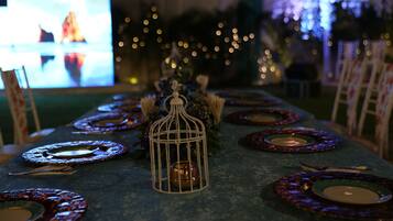 Une table dressée avec des assiettes, des couverts et une bougie, dans une pièce faiblement éclairée et décorée de guirlandes lumineuses.