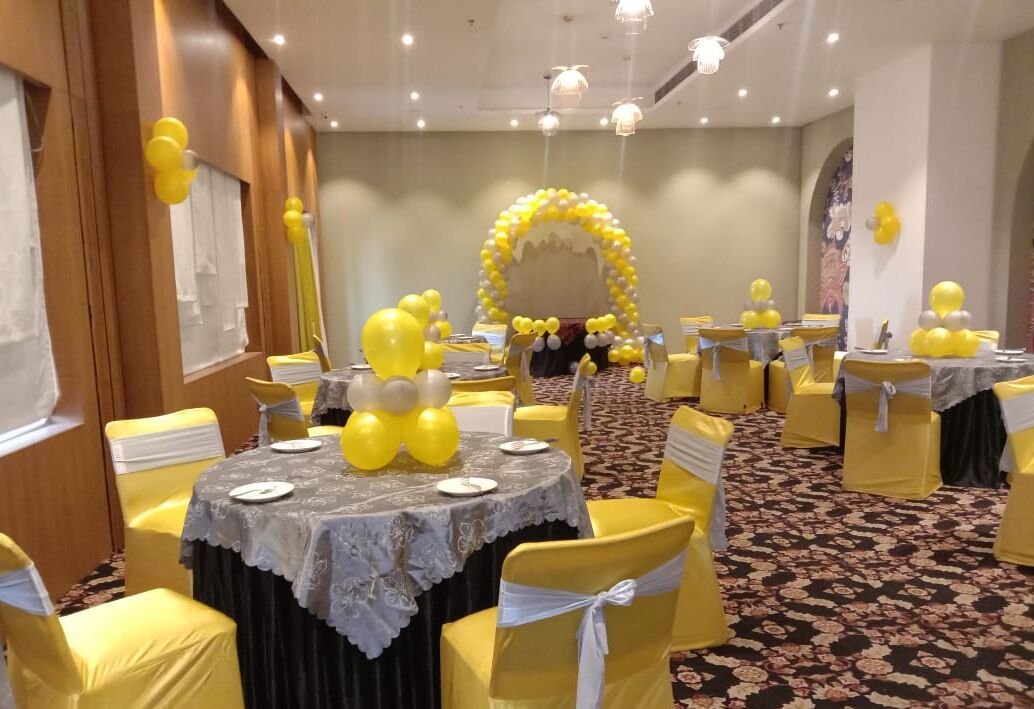 A banquet hall with round tables, yellow chairs, and a floral carpet.