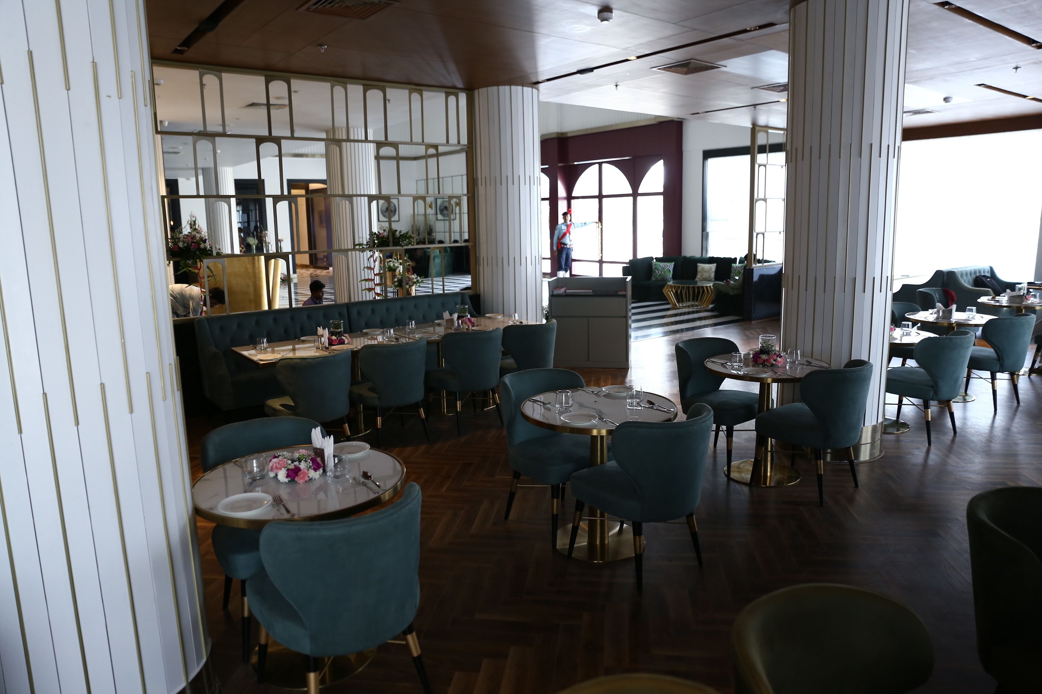 Un restaurante espacioso con mesas redondas y sillas azules, una zona de bar y amplios ventanales con vistas.