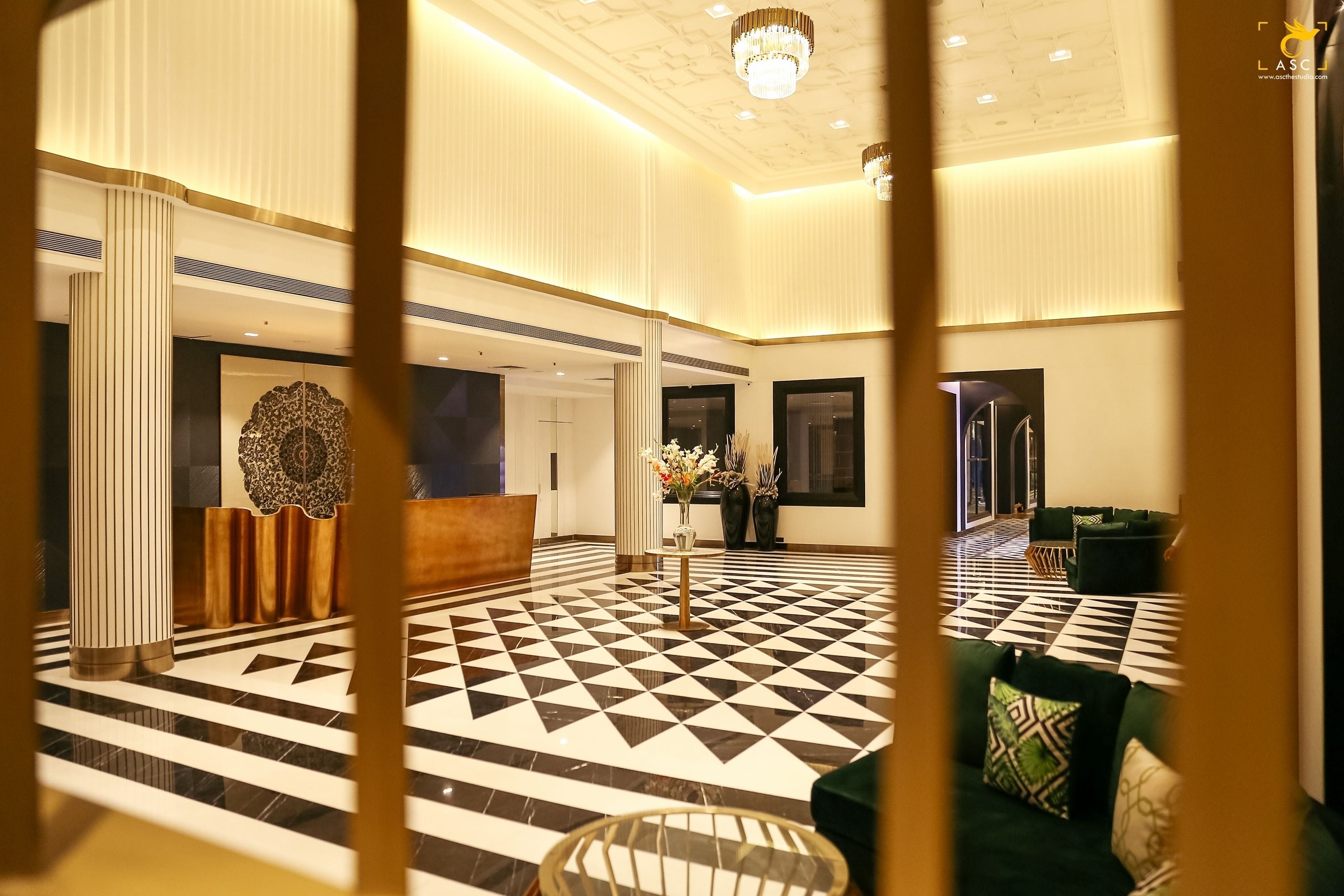 A lobby with a geometric patterned floor, a reception desk, and a seating area with green sofas.