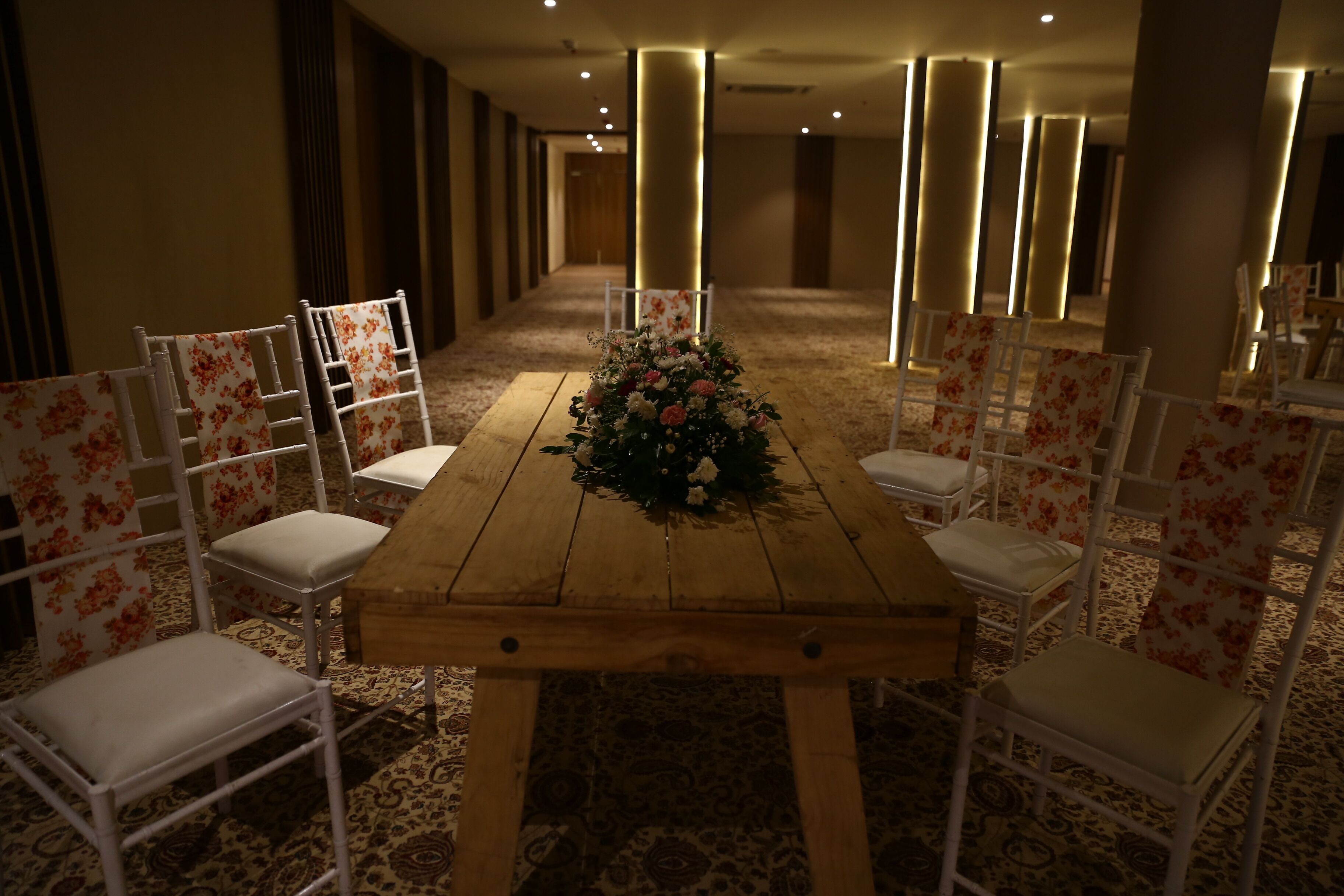 A conference room with a wooden table, white chairs, and a floral centerpiece.