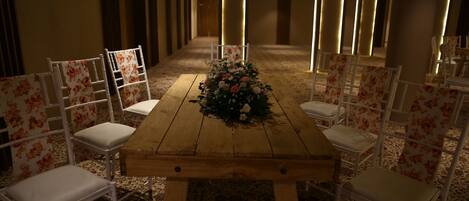 A conference room with a wooden table, white chairs, and a floral centerpiece.