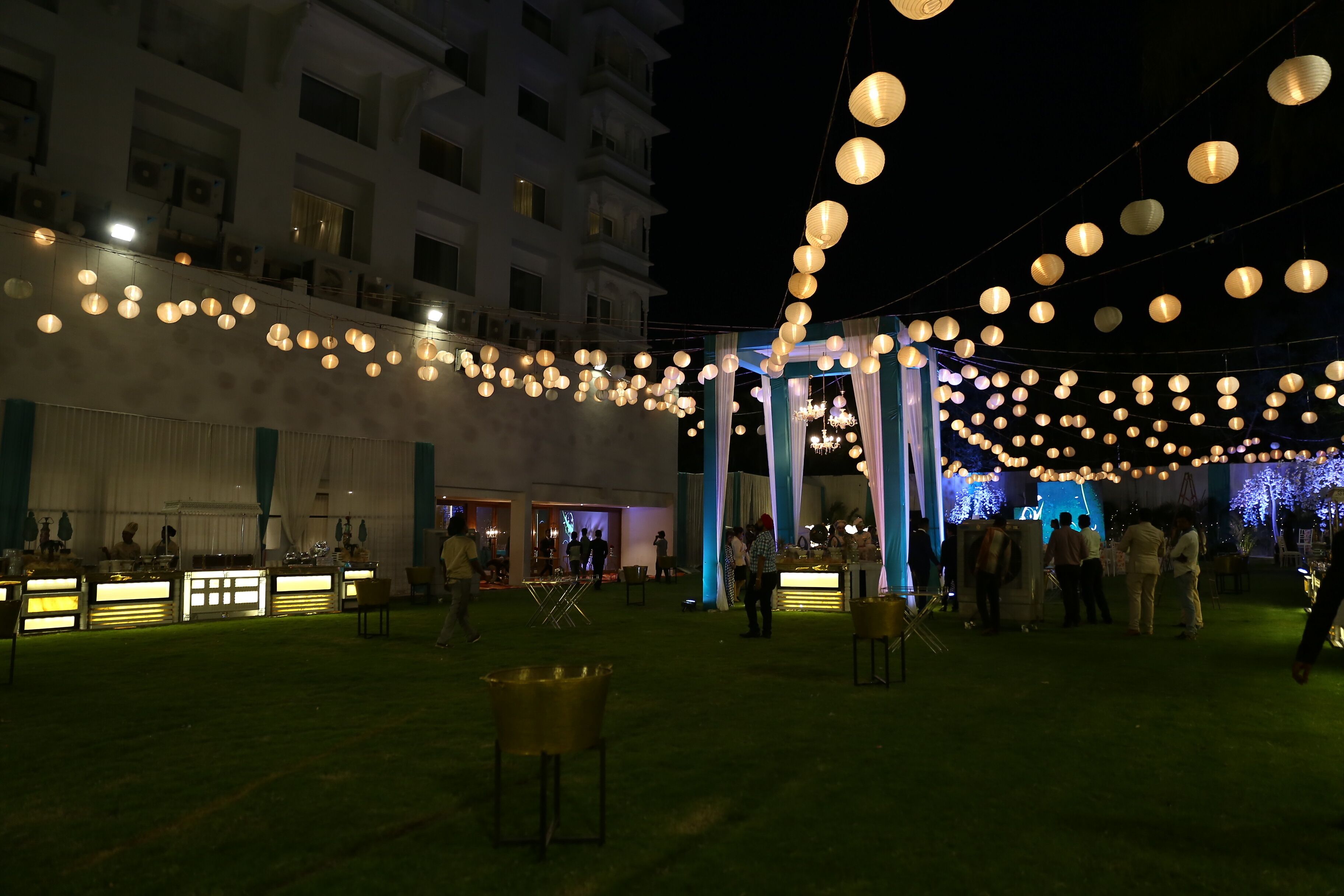 An outdoor event space with string lights, tables, and a stage area.