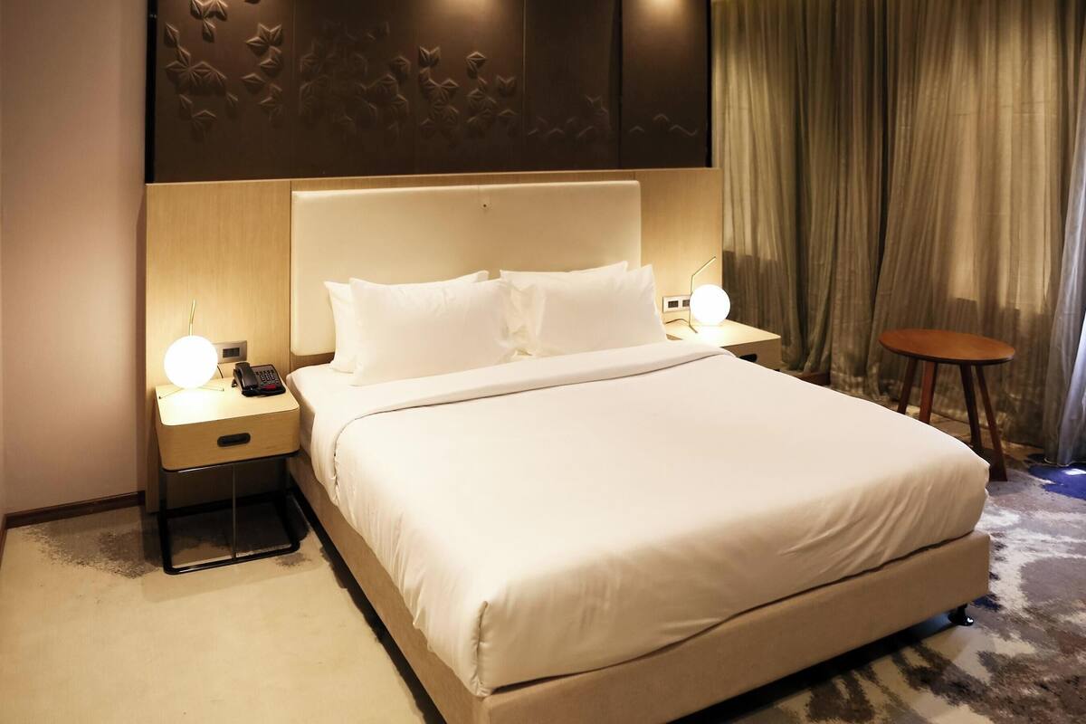 Una habitación de hotel con una cama grande, mesitas de noche con lámparas, una pequeña mesa redonda y una cortina.