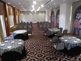 Un salón de conferencias con mesas redondas, sillas y piso alfombrado.