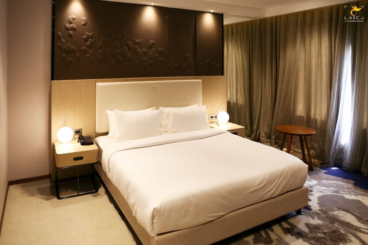 Una habitación de hotel con una cama grande, mesitas de noche con lámparas, una pequeña mesa redonda y un panel decorativo en la pared.