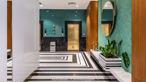 Eine moderne Hotelhalle mit einer türkisblauen Wand, einem großen Spiegel und einem schwarz-weißen, gemusterten Boden.