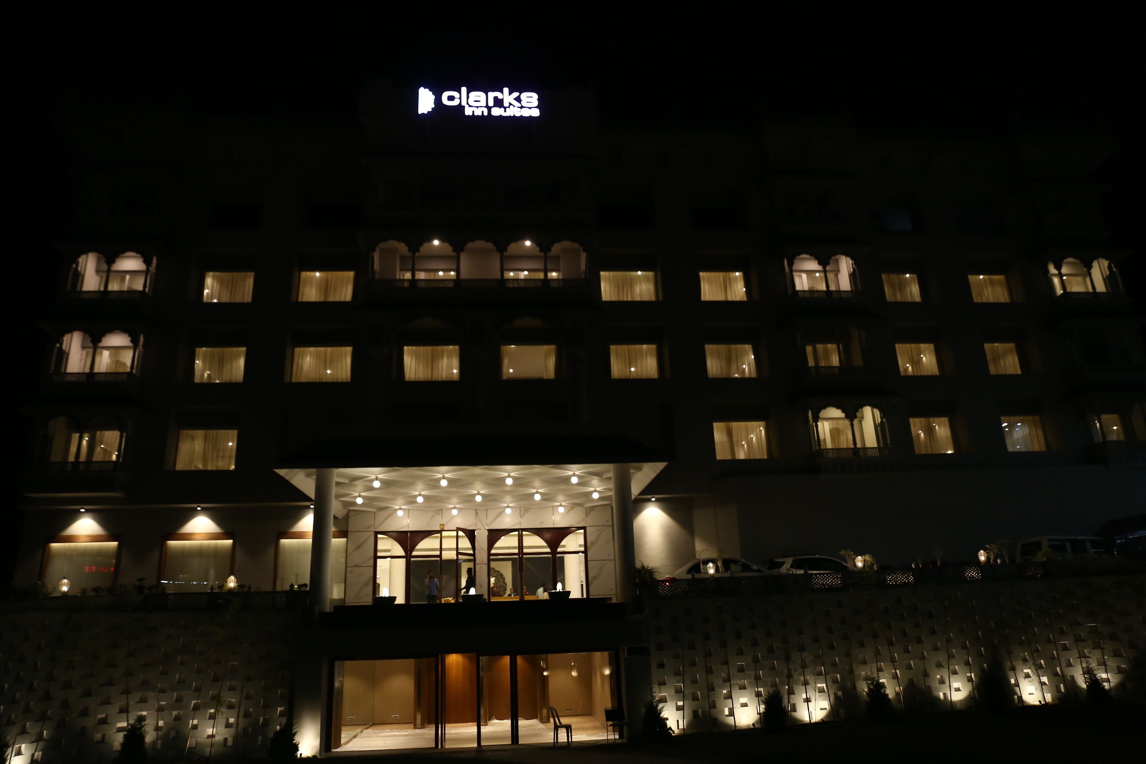 A hotel with a prominent sign reading "Clarke's Inn Suites" at night. The building features multiple balconies and large windows.