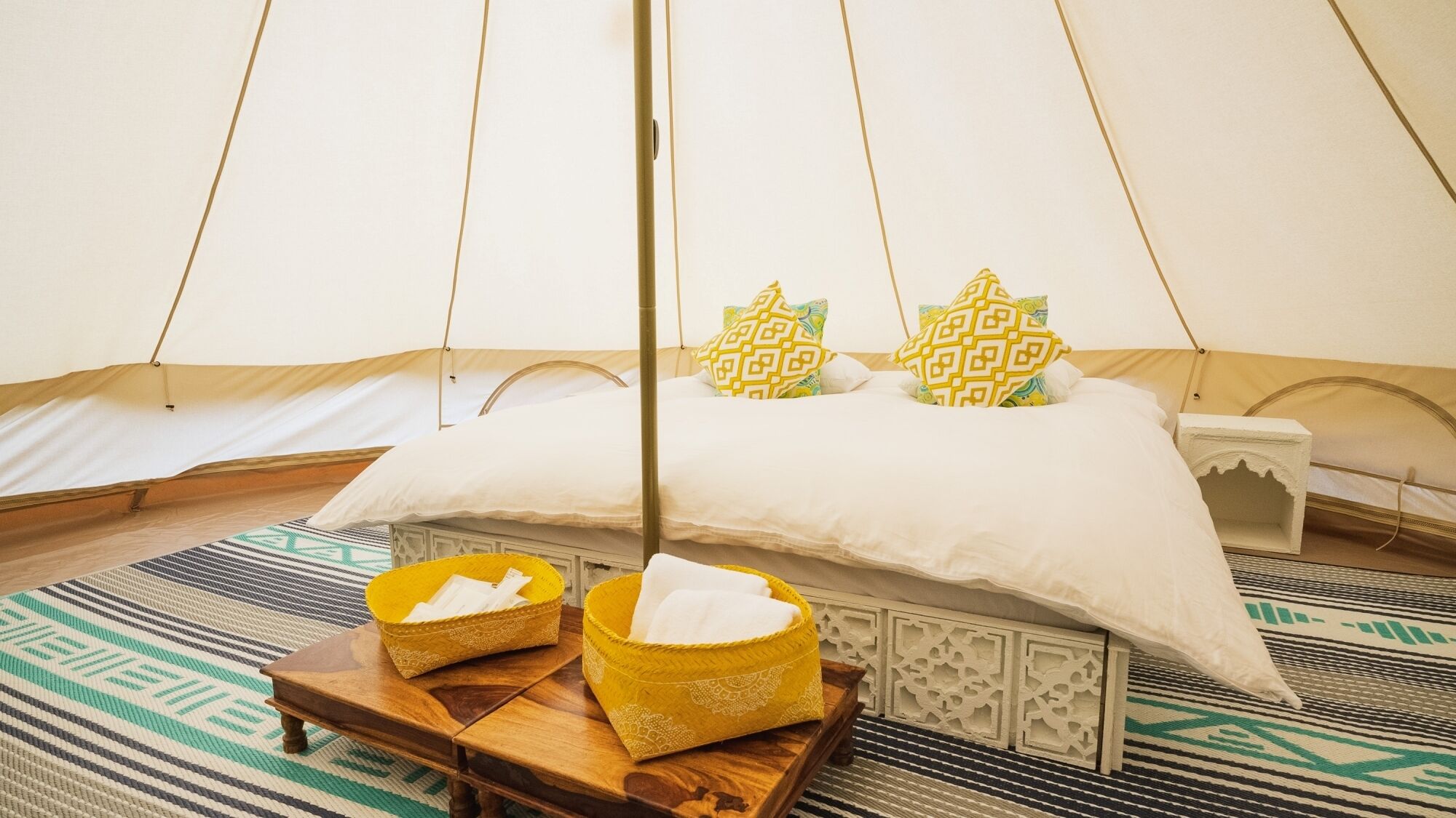 A tented room with a bed, pillows, a tray with towels, and a patterned rug.