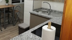 A compact kitchen with a sink, countertop, and a small dining area with a chair and table.