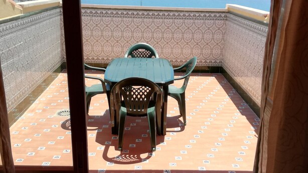 A covered outdoor seating area with a table and chairs, patterned floor tiles, and a view of the sea.