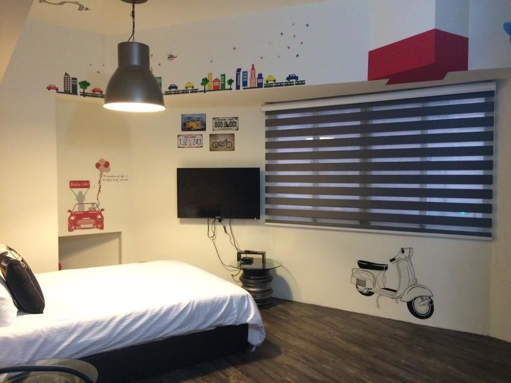 A bedroom with a bed, a wall-mounted TV, a window with blinds, and a scooter decal.