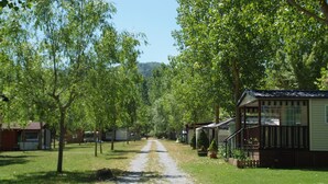 A gravel path leading through a park with trees and a row of cabins. - Camping Los Cameros (Villoslada de Cameros)