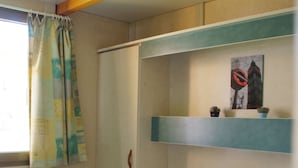 A small, compact room with a bunk bed, a window with curtains, and a shelf with a small item on it. - Camping Los Cameros (Villoslada de Cameros)