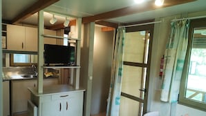 A compact kitchen with a built-in TV, a small dining area with a table and chairs, and a window with curtains. - Camping Los Cameros (Villoslada de Cameros)