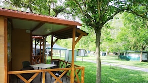 A wooden deck with a table and chairs, surrounded by a covered area with a roof. - Camping Los Cameros (Villoslada de Cameros)