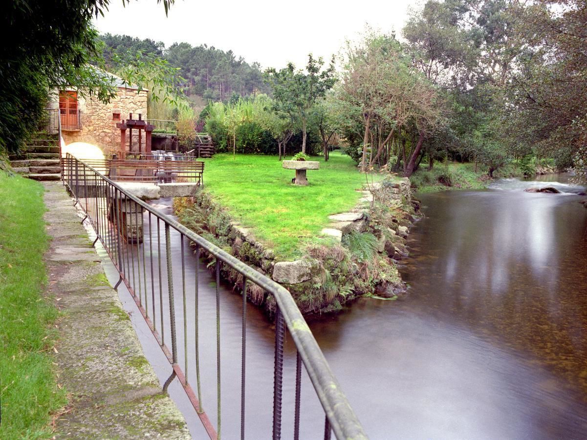 A stone building with a wooden staircase, a grassy area with a stone table, and a calm river.