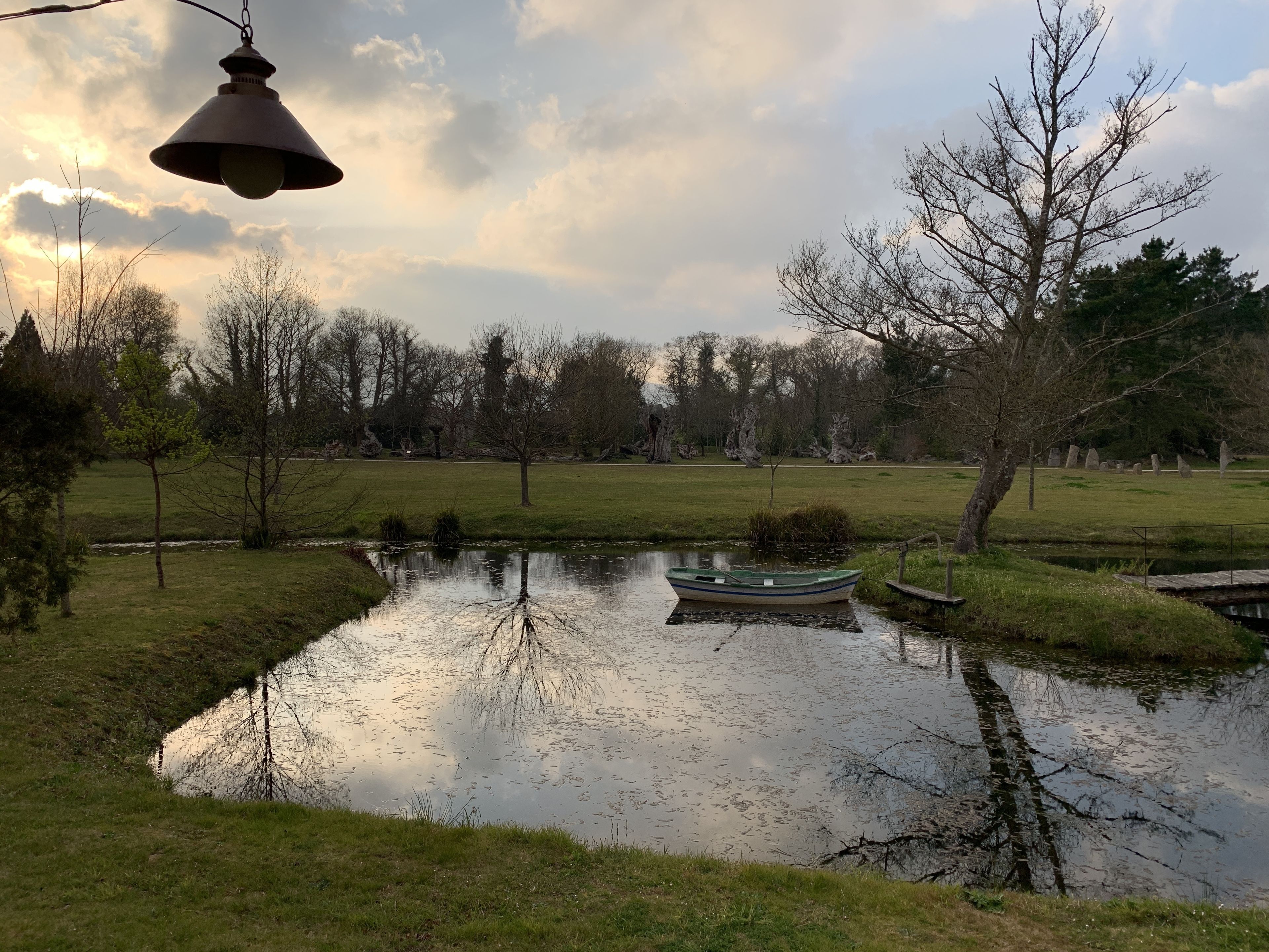 Un étang paisible avec un petit bateau, entouré de prairies et d’arbres.