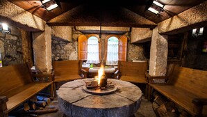 Una habitación con suelo de piedra, bancos de madera y una chimenea de piedra en el centro.